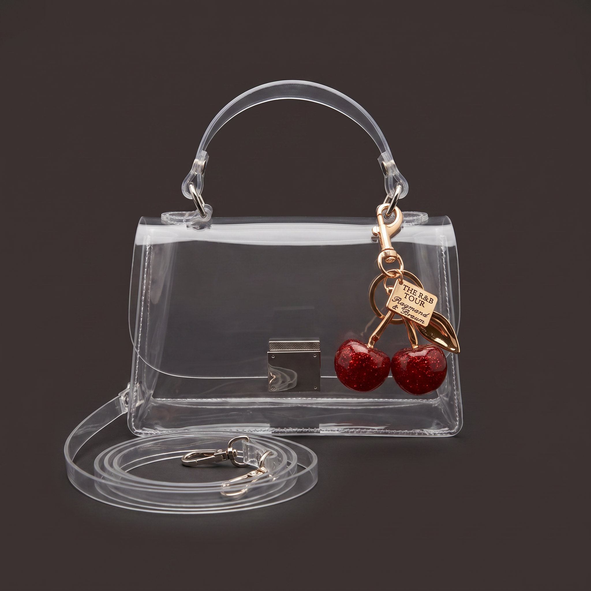 Image of Clear crossbody stadium bag with cherry charm, top handle detail on dark background and detachable strap
