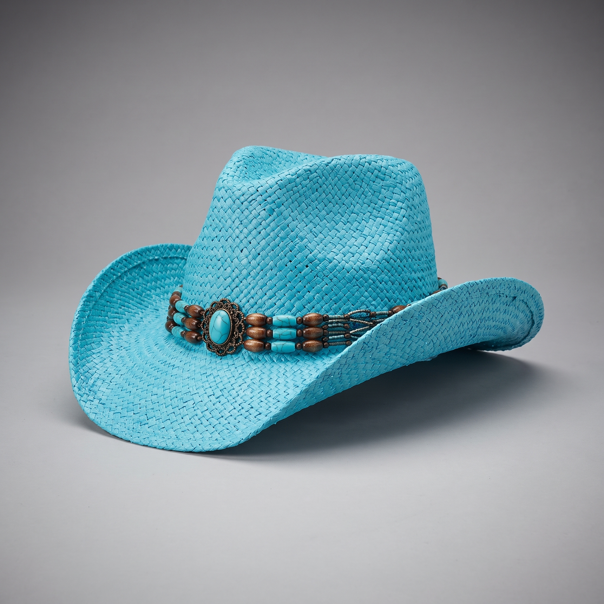 Image of A bright turquoise straw cowboy hat with a decorative band featuring turquoise, brown beads, and a silver-toned central medallion, photographed on a neutral gray background.