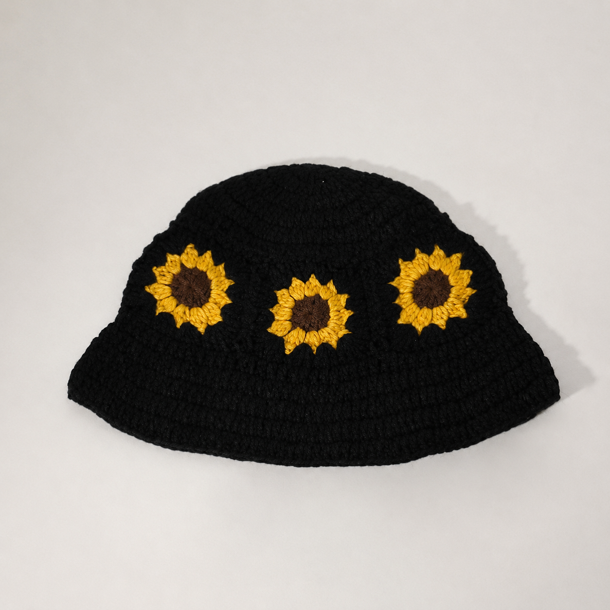 Image of A black crocheted bucket hat featuring three embroidered sunflower motifs on the front, displayed against a plain light gray background.