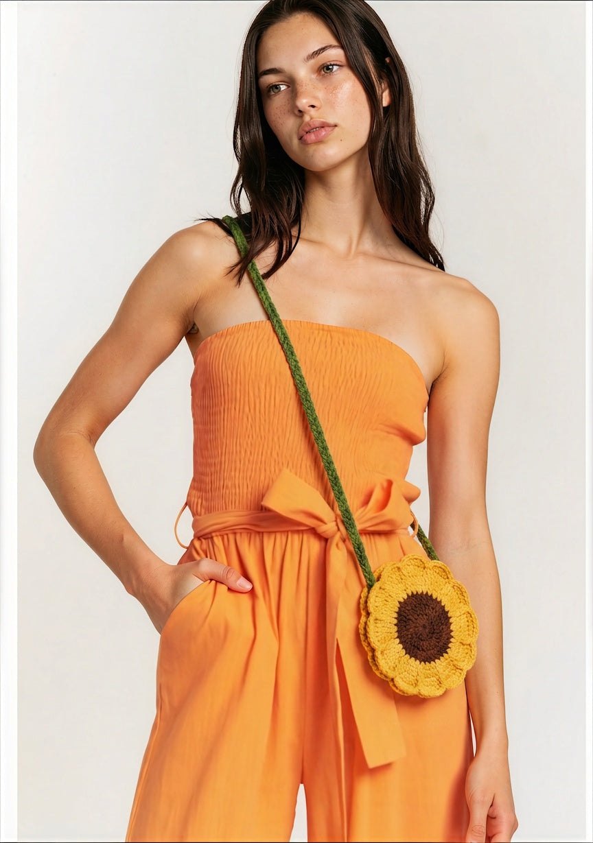 Image of A woman carrying a crocheted sunflower-shaped crossbody bag with a green strap, against a plain light background.