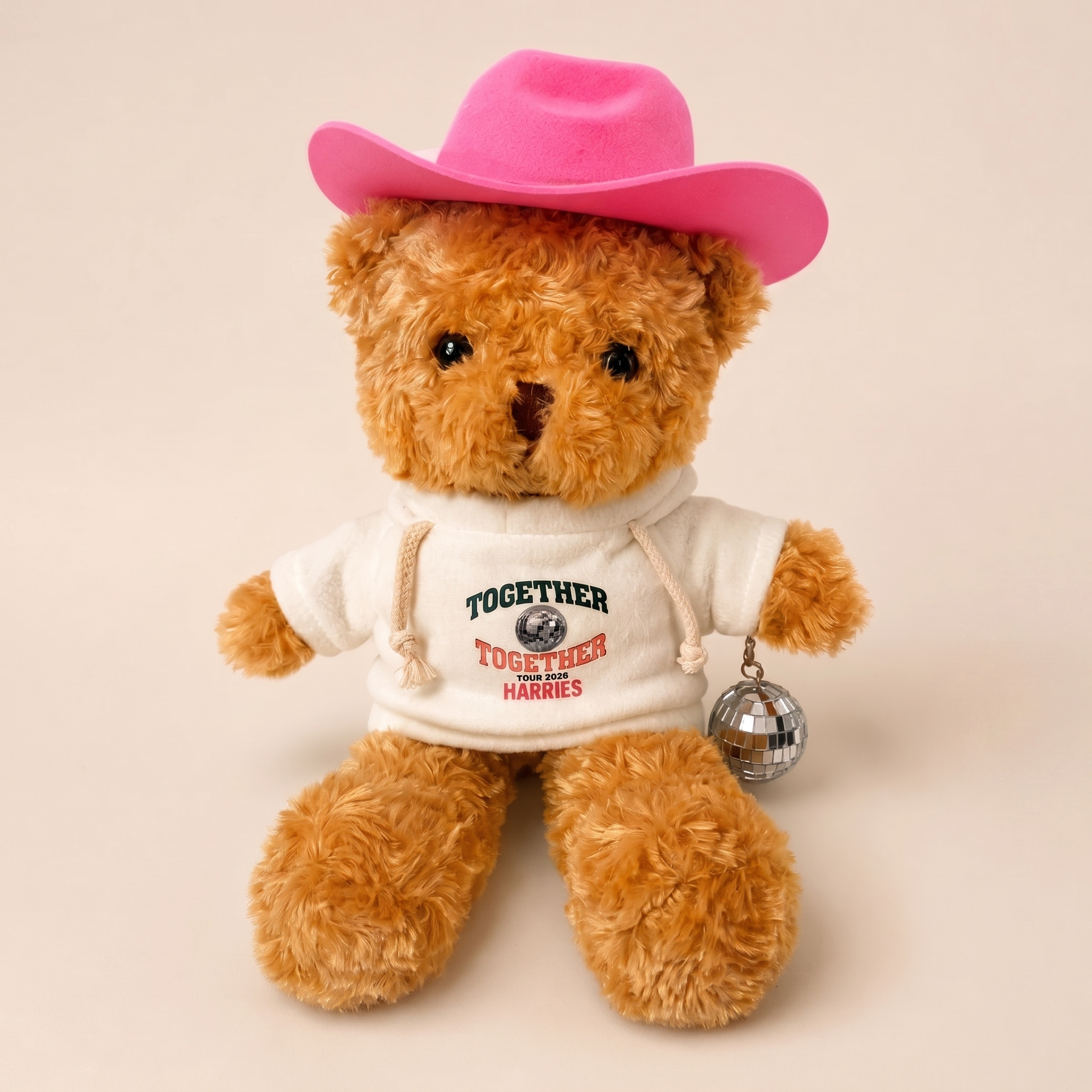 Image of A plush teddy bear wearing a bright pink cowboy hat, a white graphic sweatshirt that reads 'TOGETHER TOGETHER HARRIS,' and a small silver disco ball accessory, photographed against a plain warm beige background.