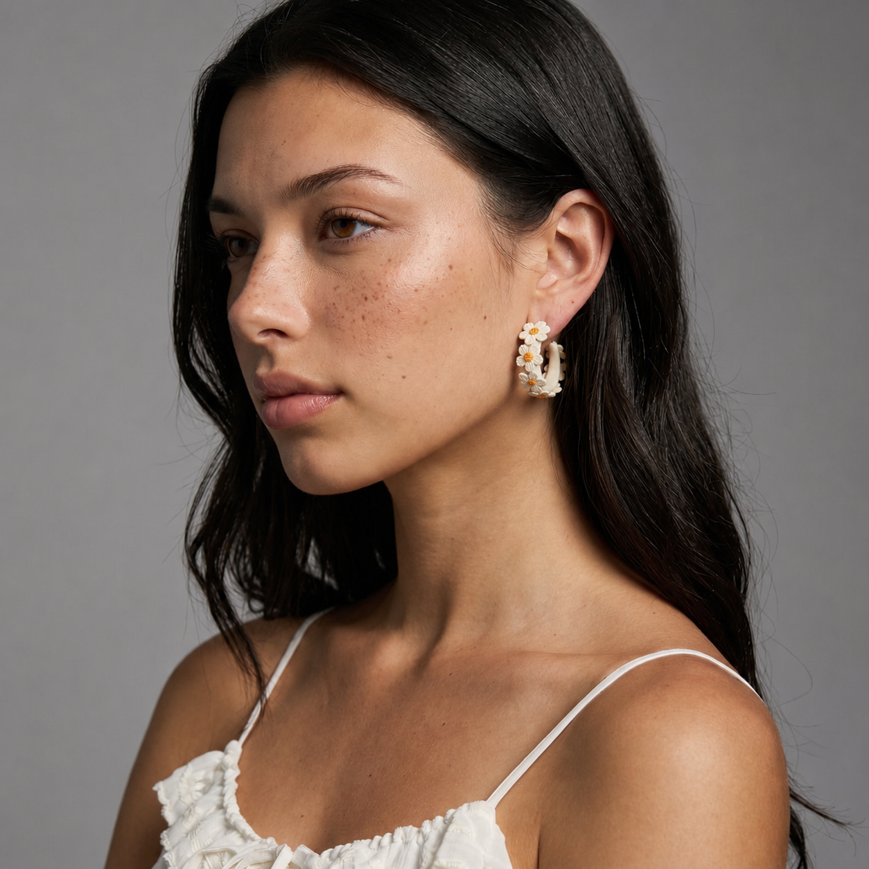 Image of Side view of woman wearing Ivory White embroidered daisy hoop earrings, studio background