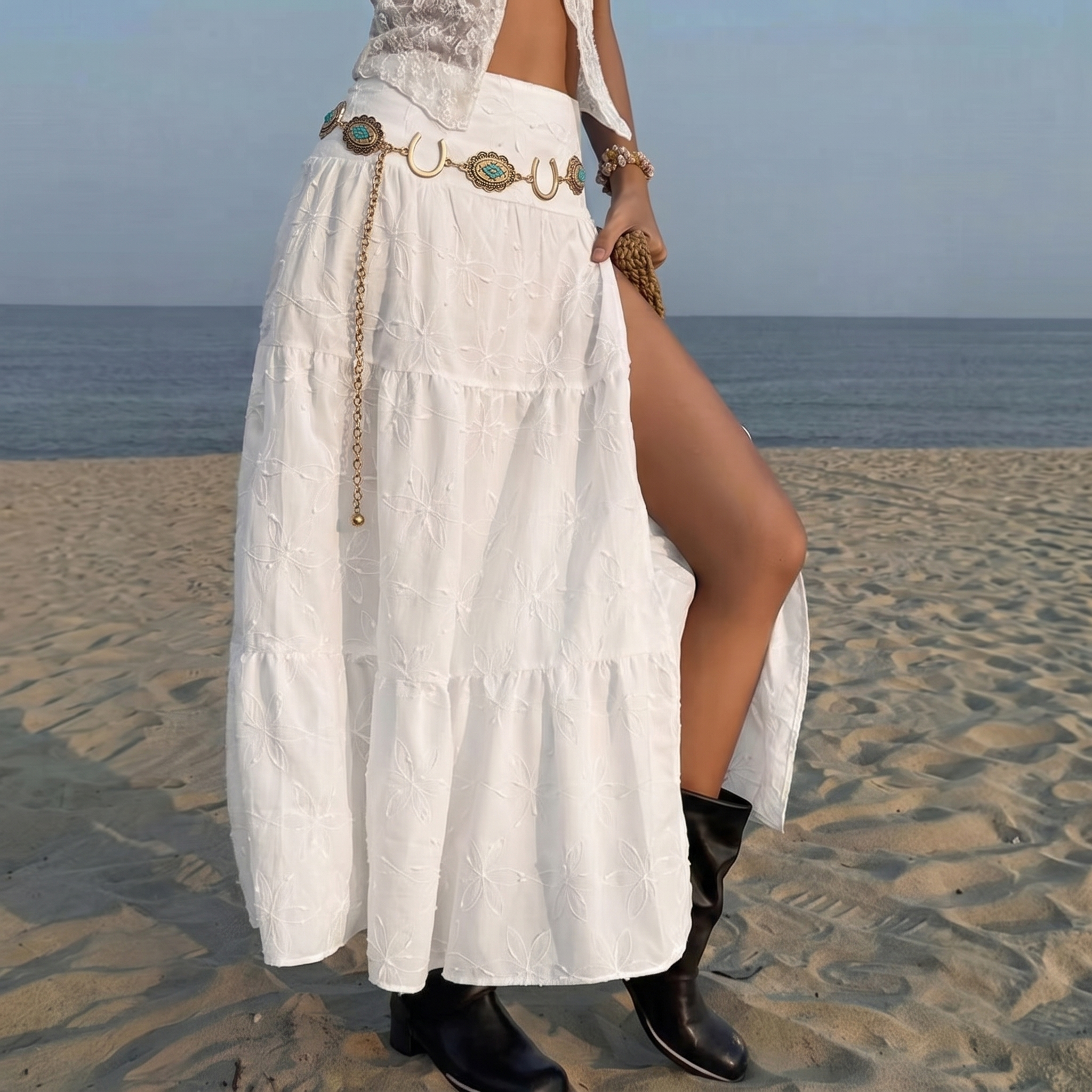 Image of Woman wearing a cowgirl belt with antique gold horseshoe and turquoise concho medallions over a white dress with black cowgirl boots on the beach