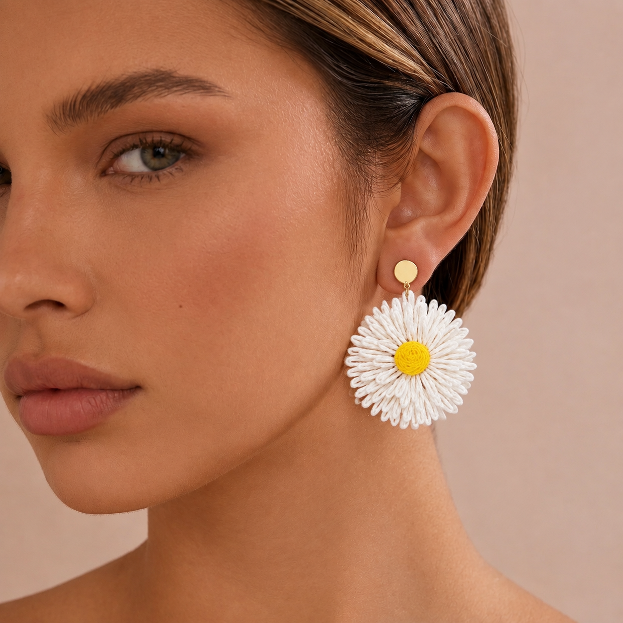 Image of A close-up of a woman wearing a large white daisy drop earring with a yellow center and a gold stud, against a soft beige background.