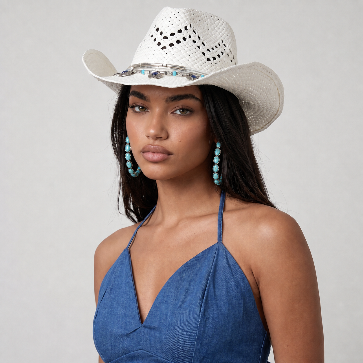 Image of A woman wearing a white woven cowboy hat with silver and turquoise accents, a blue halter top, and matching turquoise drop earrings, photographed against a light gray studio background.