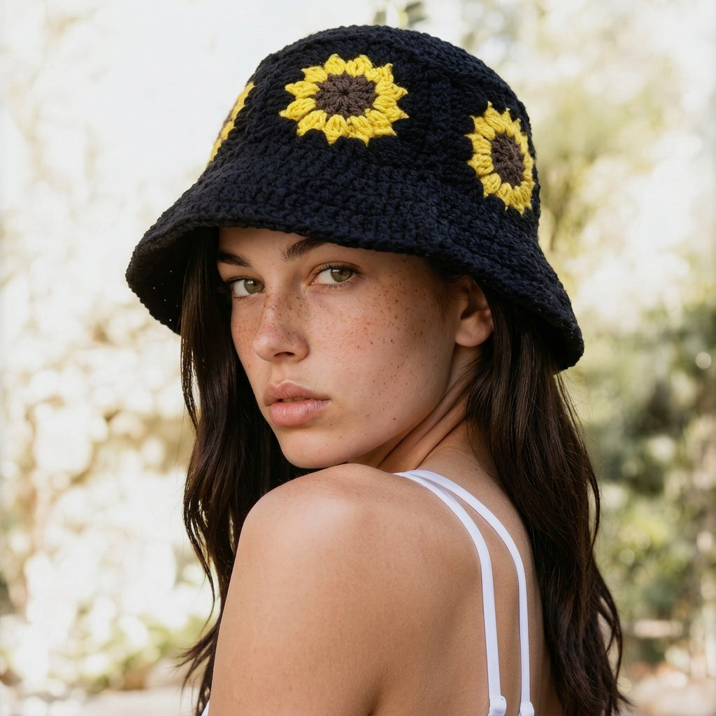 Image of A woman wearing a black crocheted bucket hat with yellow sunflower details, photographed outdoors against a softly blurred light background.