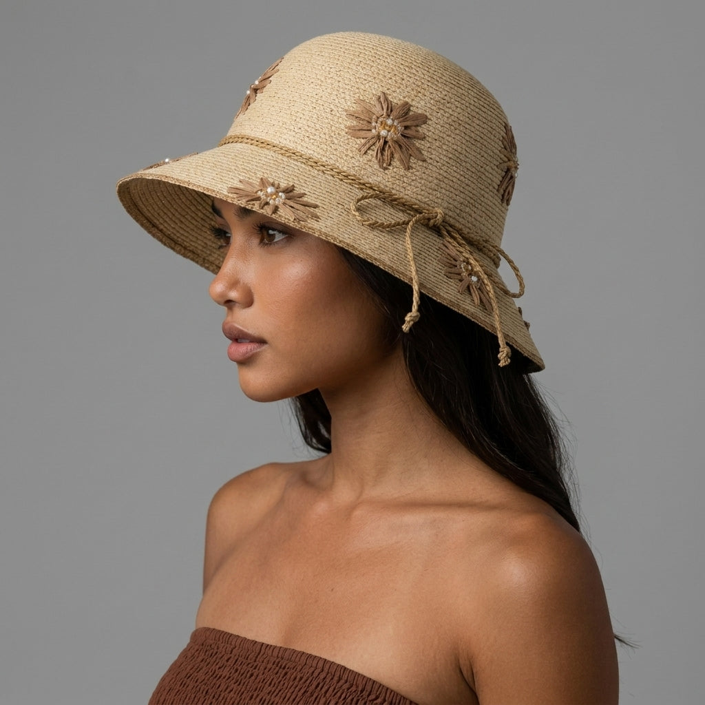 Image of A woman in profile wearing a natural straw sun hat with woven floral embellishments and a side tie, photographed against a plain gray studio background.