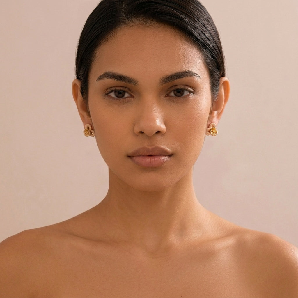 Image of A close-up portrait of a woman wearing small gold floral stud earrings against a soft beige background.