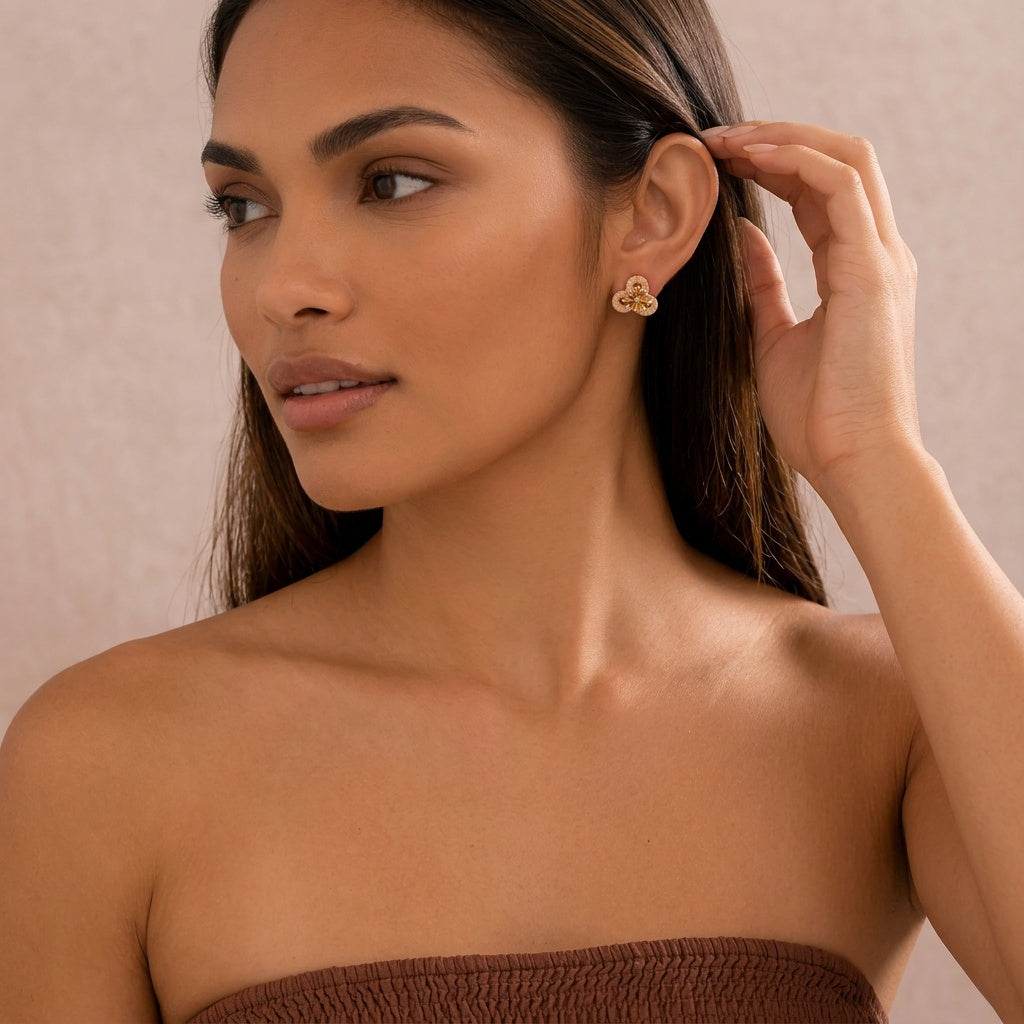 Image of A woman wearing a small gold-toned triple-leaf earring, shown in a close-up portrait against a soft beige background.