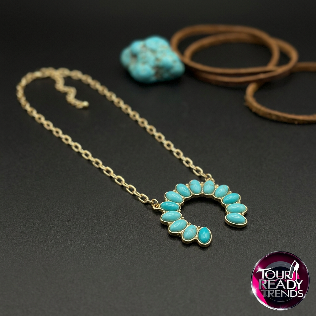 Image of Gold necklace with a crescent-shaped pendant set with turquoise-colored stones, displayed on a dark background with a small turquoise stone and brown cords in the background. A 'Tour Ready Trends' logo is visible in the bottom right corner.